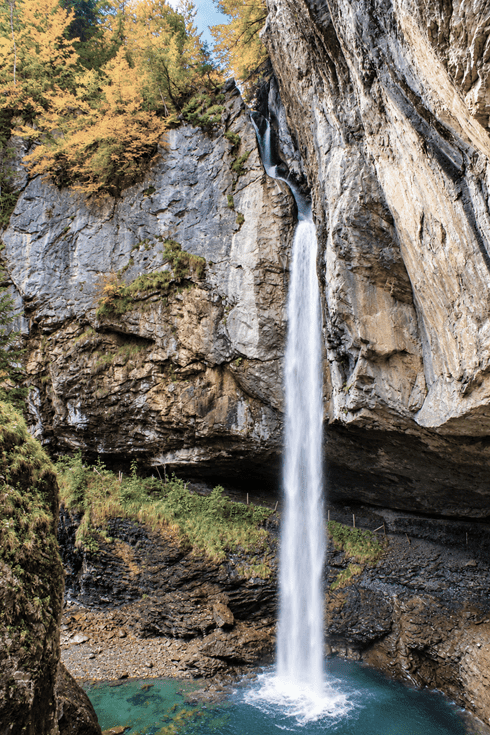 Wasserfall Berglistüber im Glarnerland mit hohem Wasserfall, steilen Felswänden, türkisblauem Wasserbecken und leuchtend gelbem Herbstlaub.